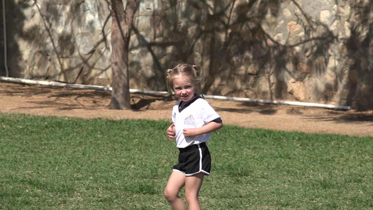 Blond young girl in a white and black sports uniform on grass.