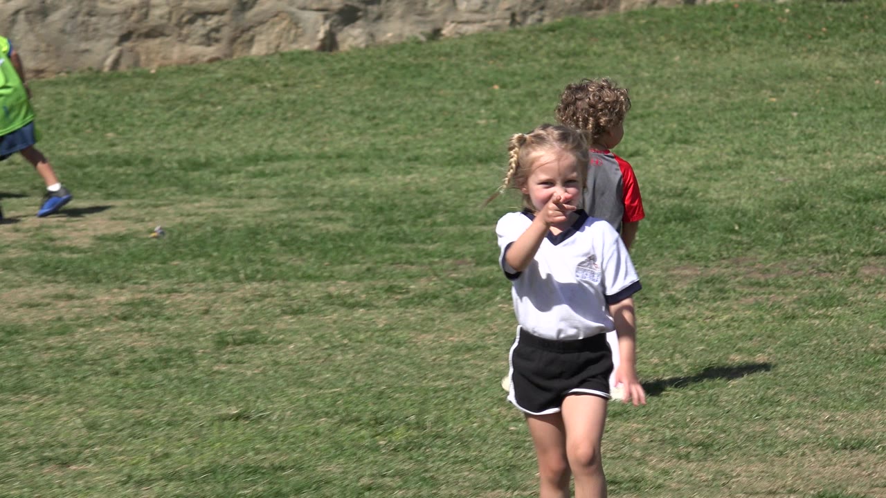 Young girl points toward the camera on a sunny grass field.