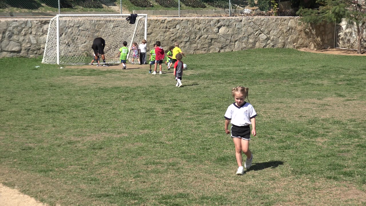 The girl remains centered on the field in Los Cabos, Mexico, with a small group of children and an adult beside the soccer goal in the background.