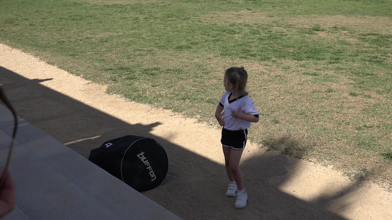 The girl remains on the outdoor steps in Los Cabos, Mexico, facing across the walkway as strong shade cuts diagonally over the concrete and grass.