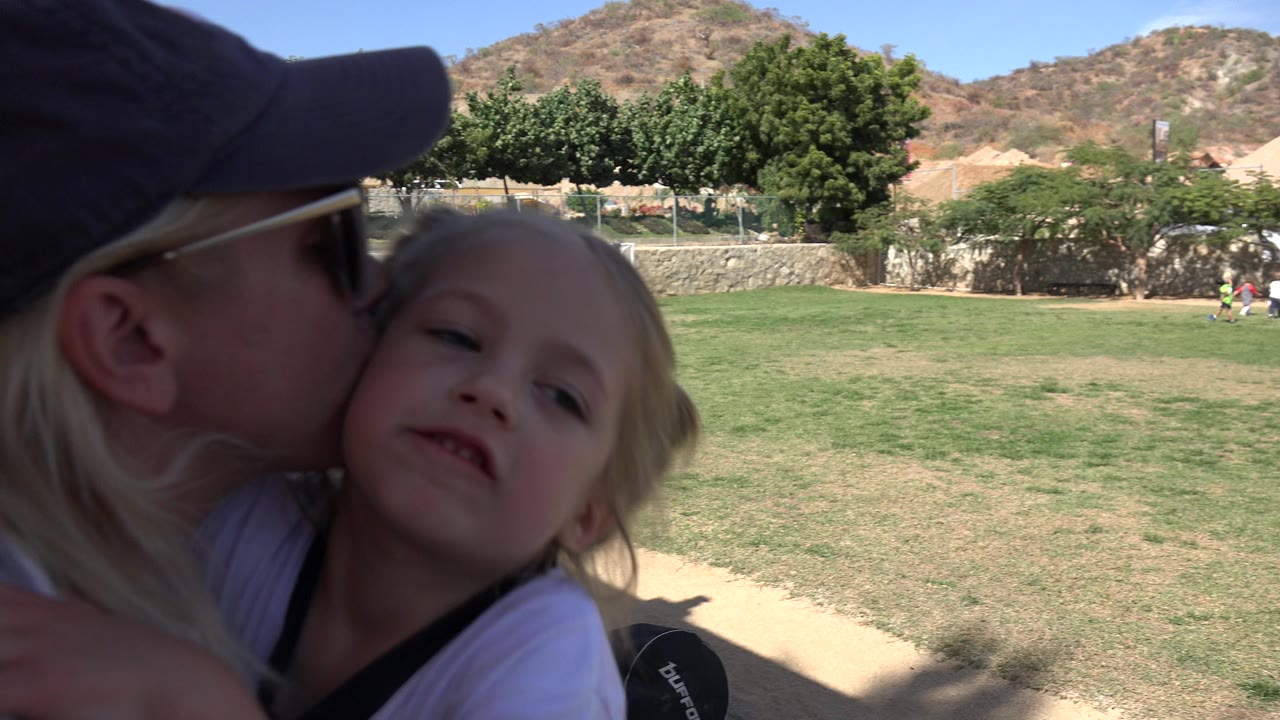Woman kisses a young girl on the cheek beside a sunny field.