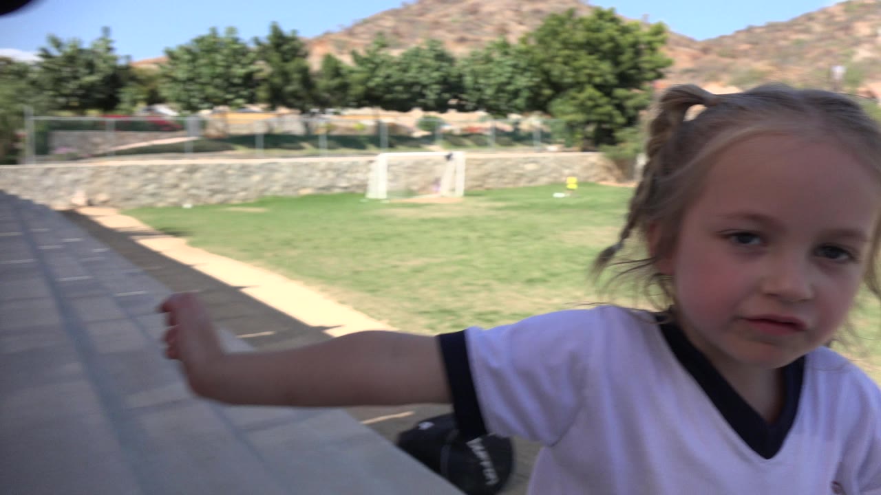 Young blonde girl close to the camera beside a soccer field.