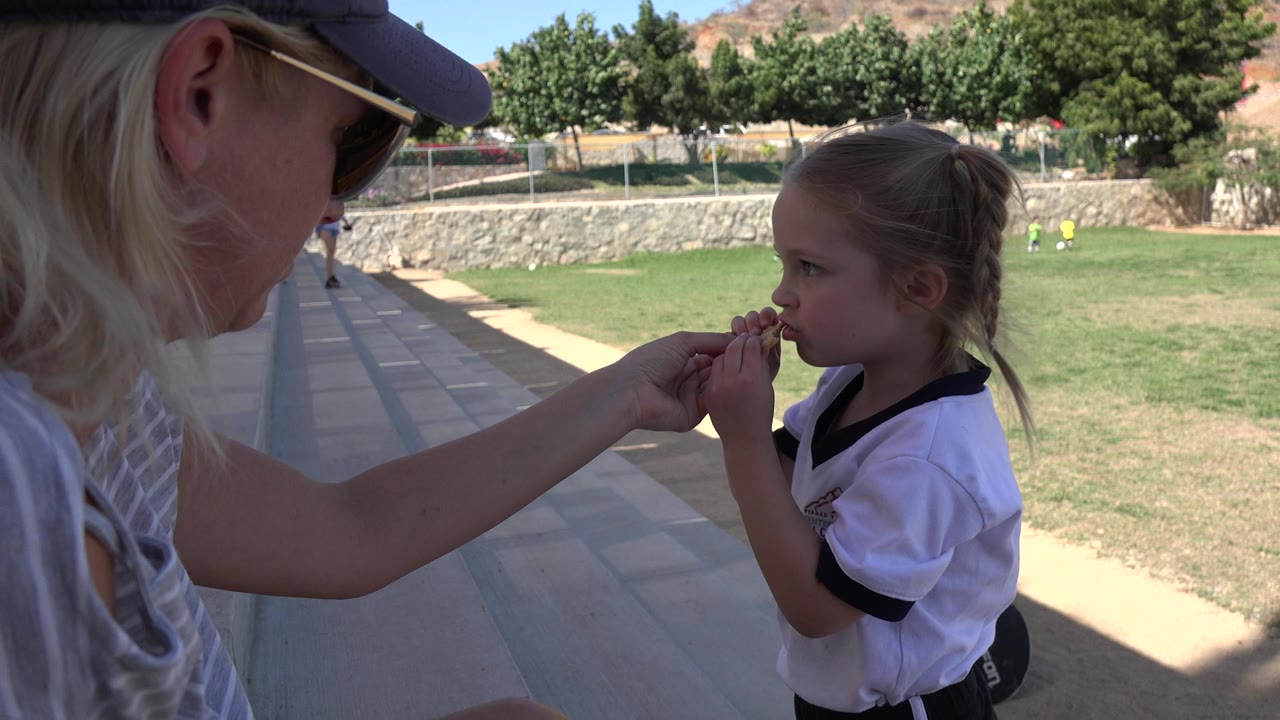 Adult and small girl face each other at the edge of a field.
