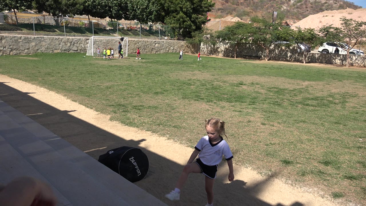 Young girl near shaded sideline with youth soccer game in the distance.