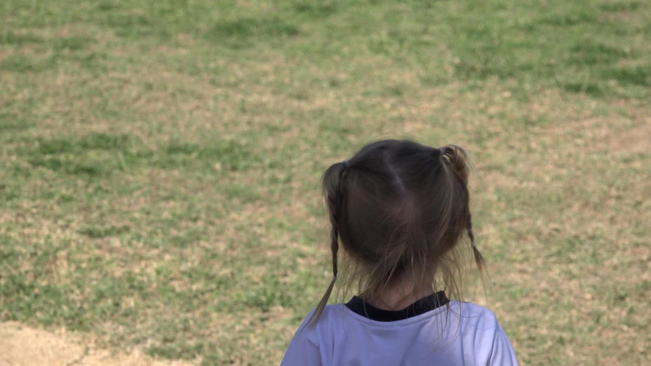One second in, the young girl remains seen from behind in Los Cabos, with loose hair strands and a white shirt visible against the open field.