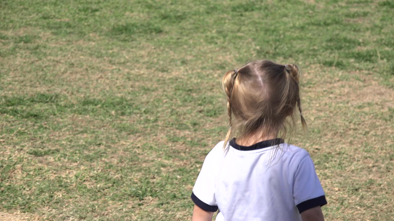 Young girl at right side of a sunlit grass field.