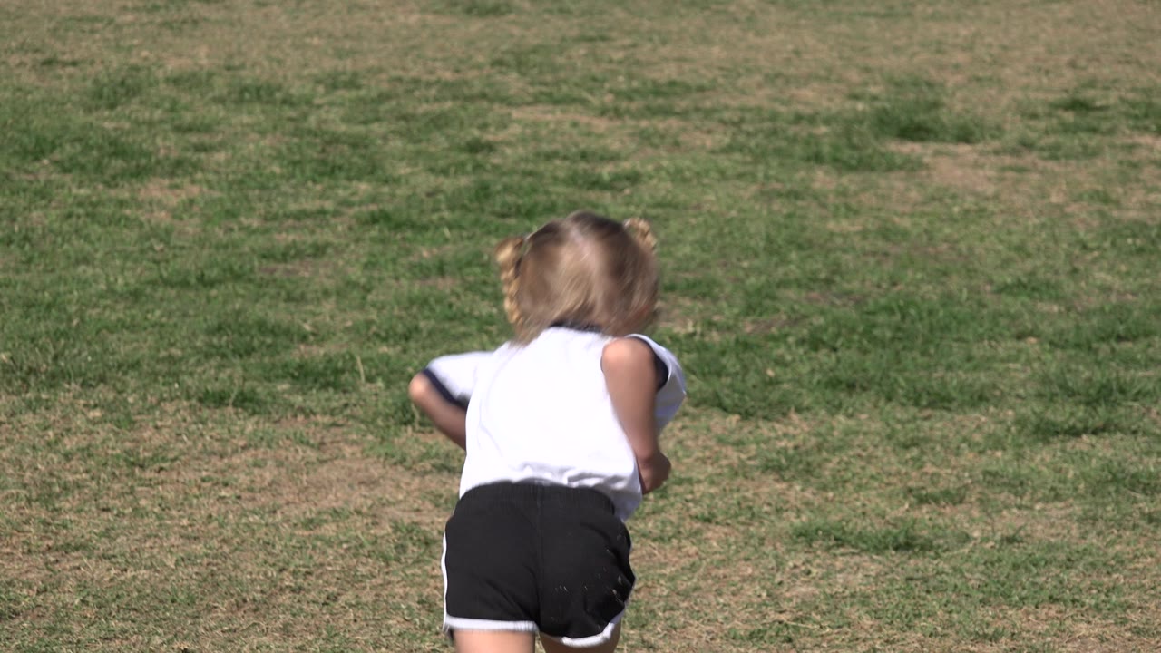 Small child running away across a grassy field.