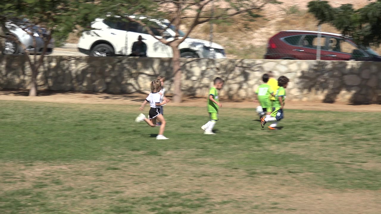 Children running on a grass soccer field near a stone wall.