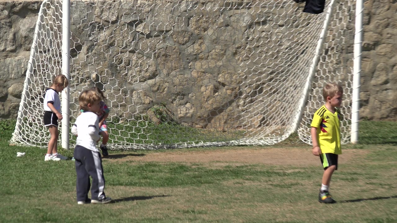A child in a yellow shirt walks in front of a white football goal while other children remain near the net in Los Cabos, Mexico.