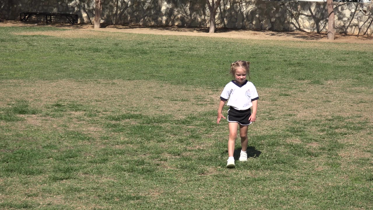 Young girl in a sports uniform standing on a grass field.