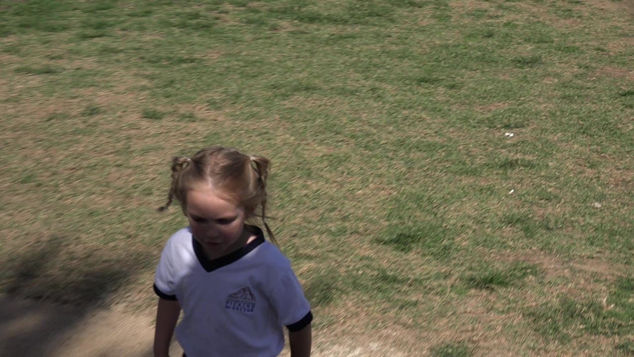 Young girl looks downward from a shaded foreground area, with patchy sunlit grass filling most of the Los Cabos frame.