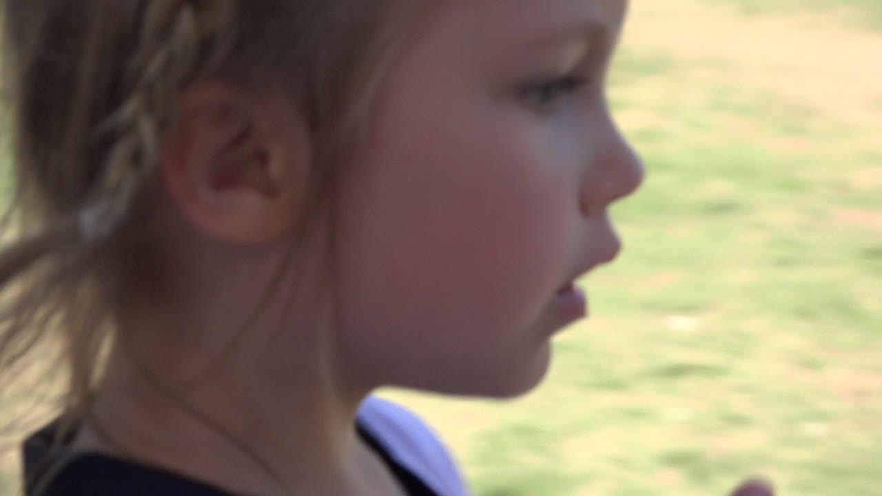 Close side profile of a young blonde girl beside a sunlit lawn.