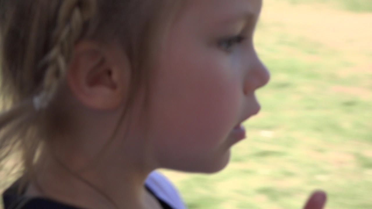 Young blonde girl in Los Cabos, Mexico, seen in close side profile as the grassy soccer area stays blurred behind her.