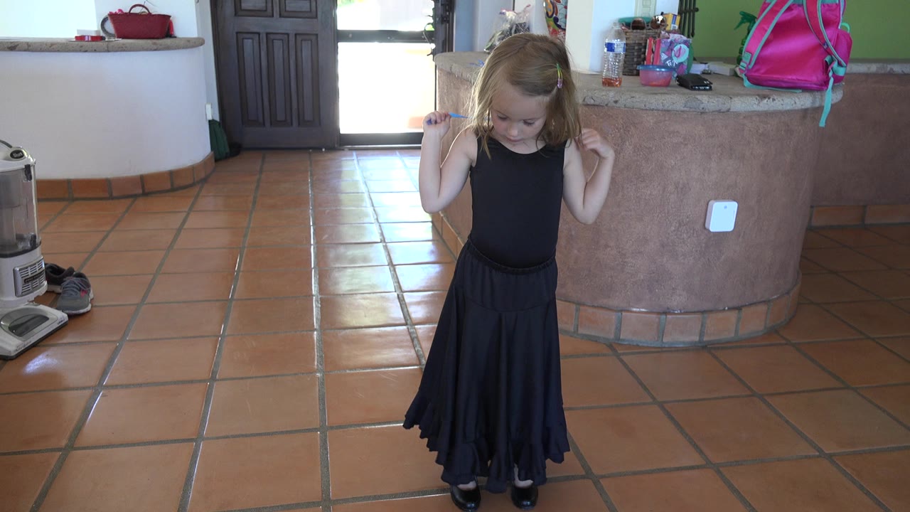 Child in a black dress holding a blue rope in a tiled kitchen.