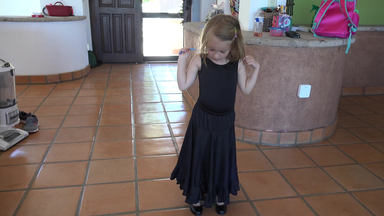In Los Cabos, Mexico, the child remains centered on the tile floor, head lowered, with the blue rope lifted near the shoulders and the curved counter behind.