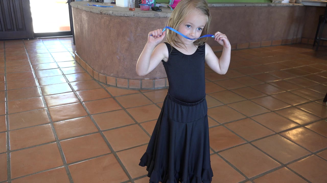 Young blond girl in a black dress holding a blue ribbon indoors.