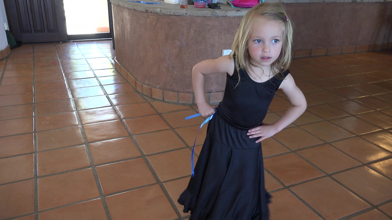 At 0:01, the girl remains near the center of the Los Cabos interior frame, holding a blue string at her side with one hand on her hip.