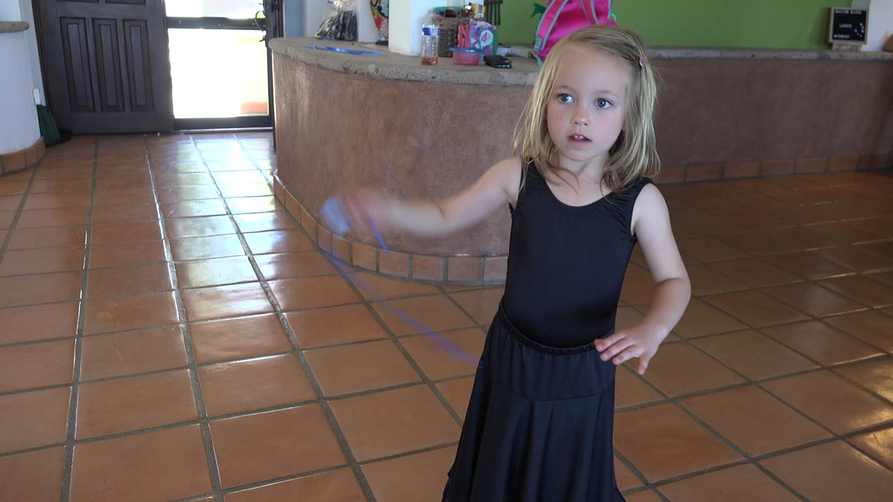 Young girl in a black dress raises a blue ribbon on a tile floor.