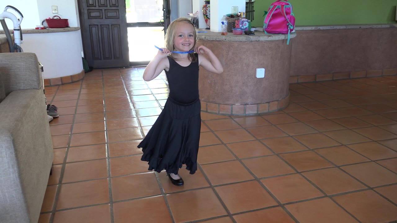 Blonde girl dancing with hands raised near her shoulders.