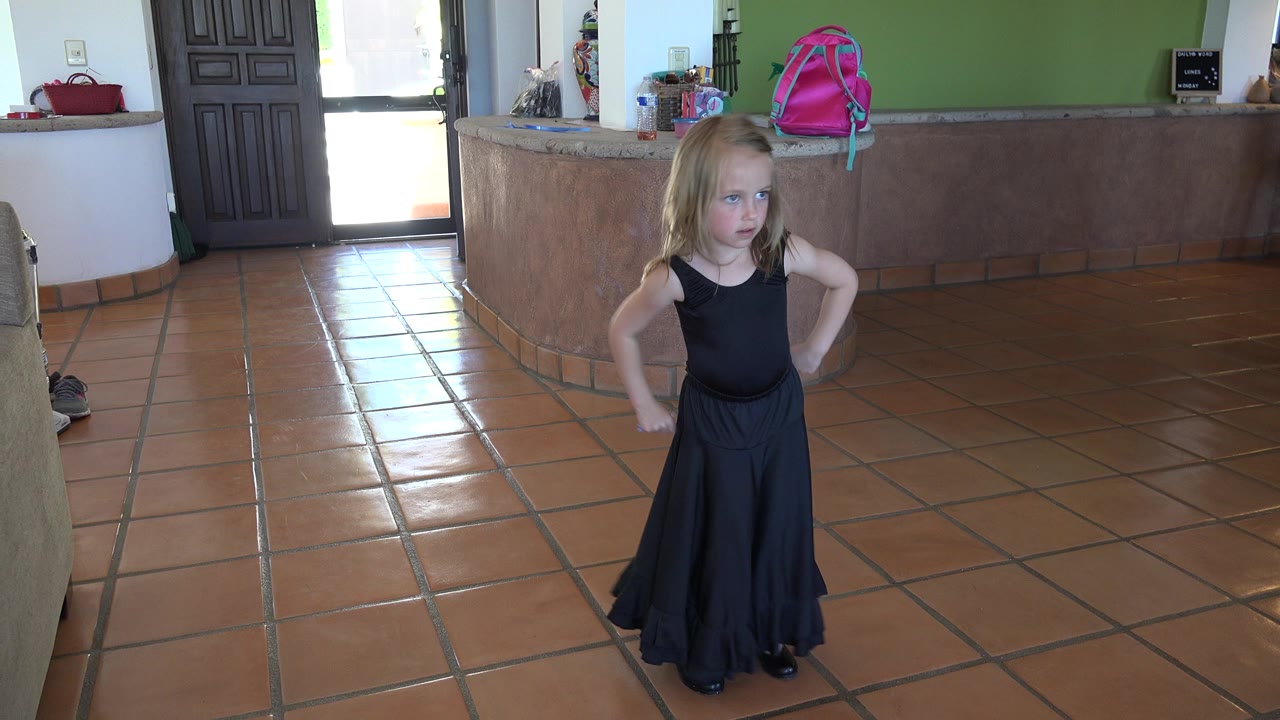 The child holds a poised dance stance near the center of the Los Cabos kitchen, with the curved counter and bright doorway behind her.