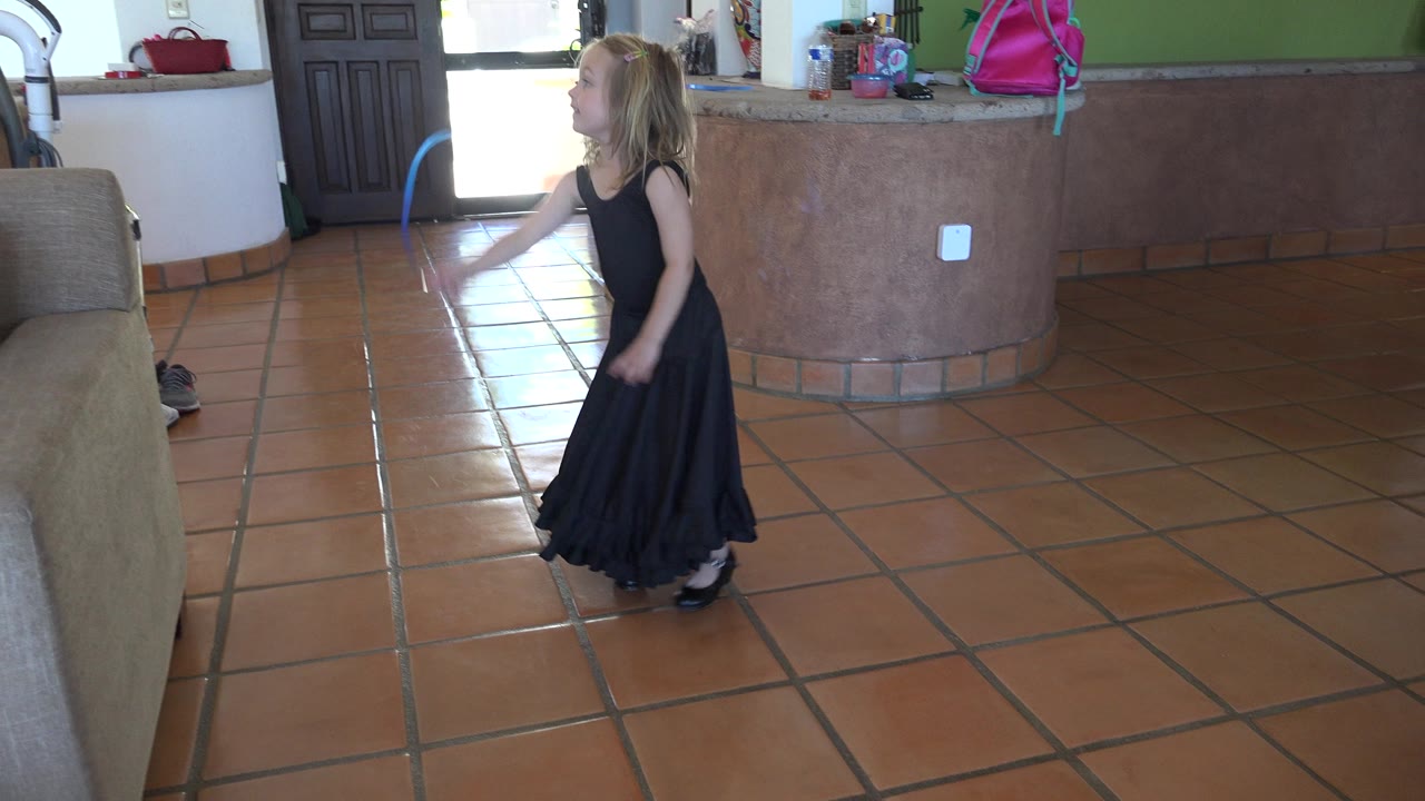 Young girl in a black dress holding a blue ribbon indoors.