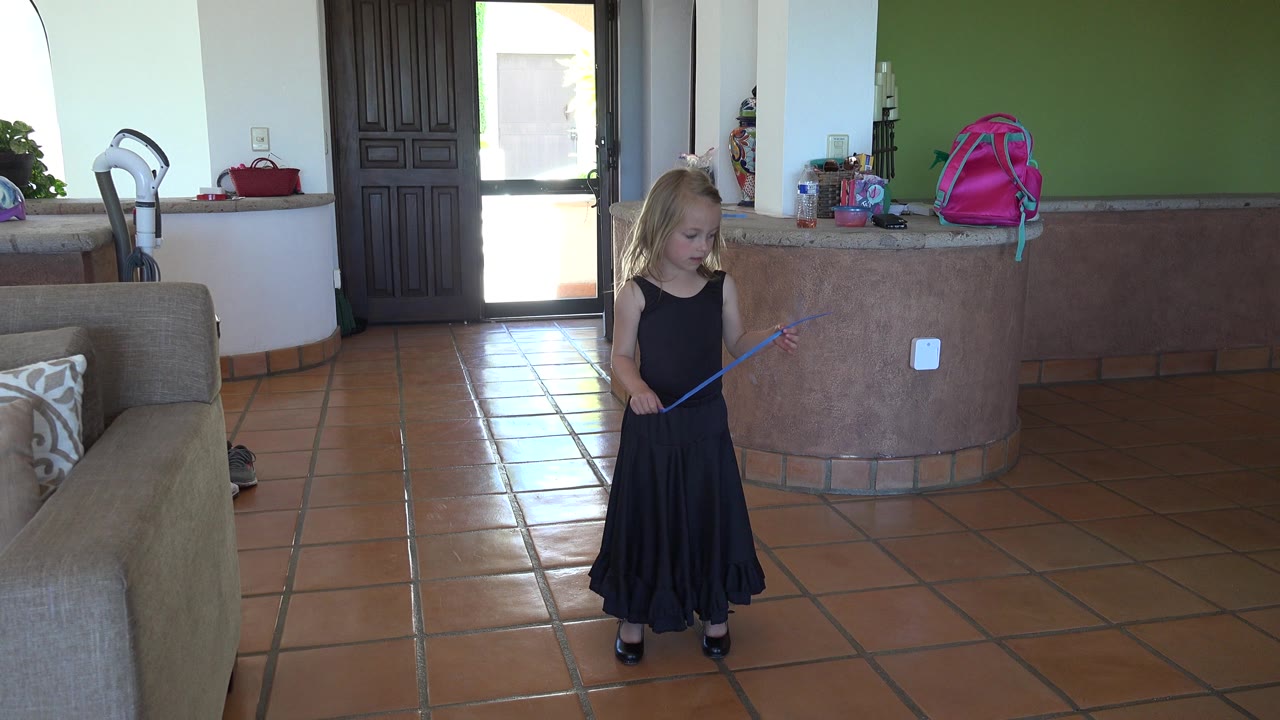 Young girl in black dress holding a blue streamer in a living room.