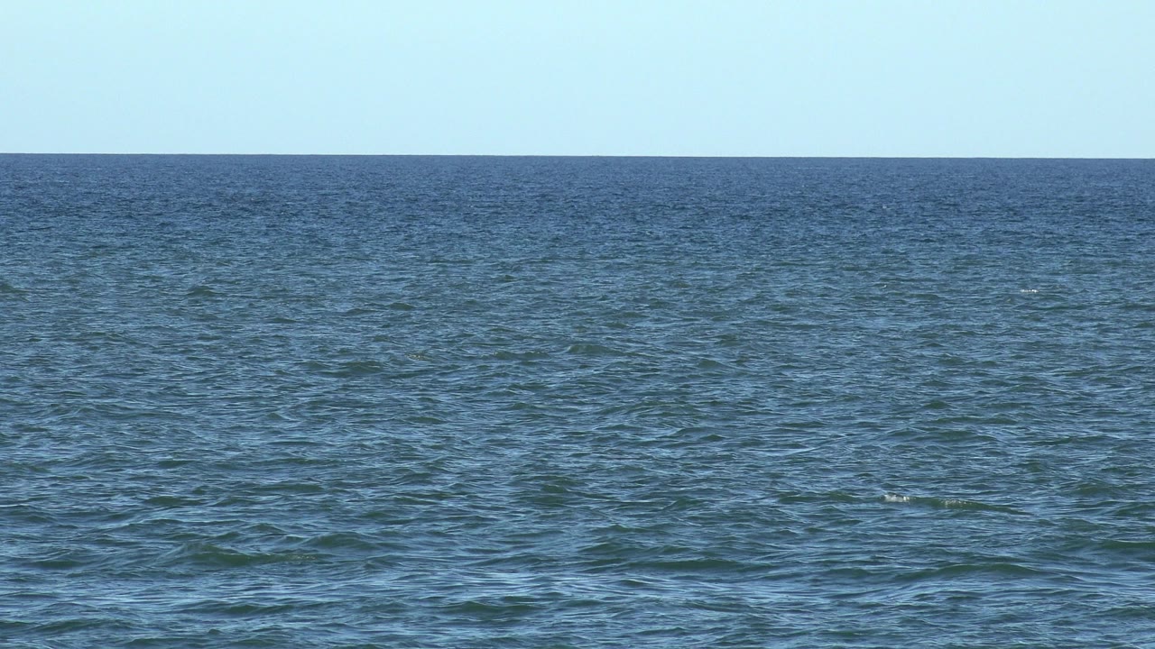 Wide Los Cabos ocean frame with slightly darker rippled water across the foreground, a clear horizon, and no visible people.