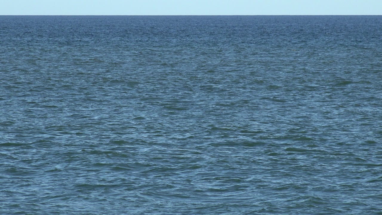 Wide Los Cabos ocean view with blue-green water, a level horizon, pale sky, and no visible people at the start of the clip.