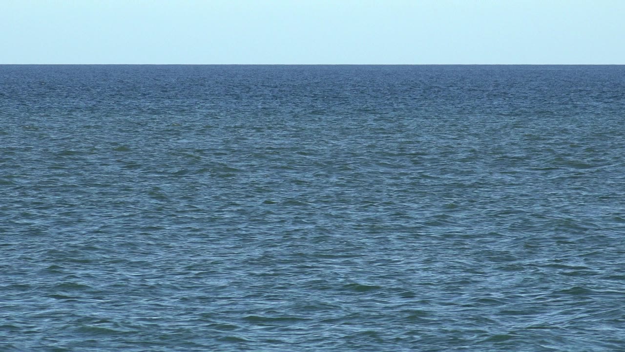 Opening frame of blue ocean water in Los Cabos, Mexico, with small ripples, a level horizon, pale sky, and no visible people.