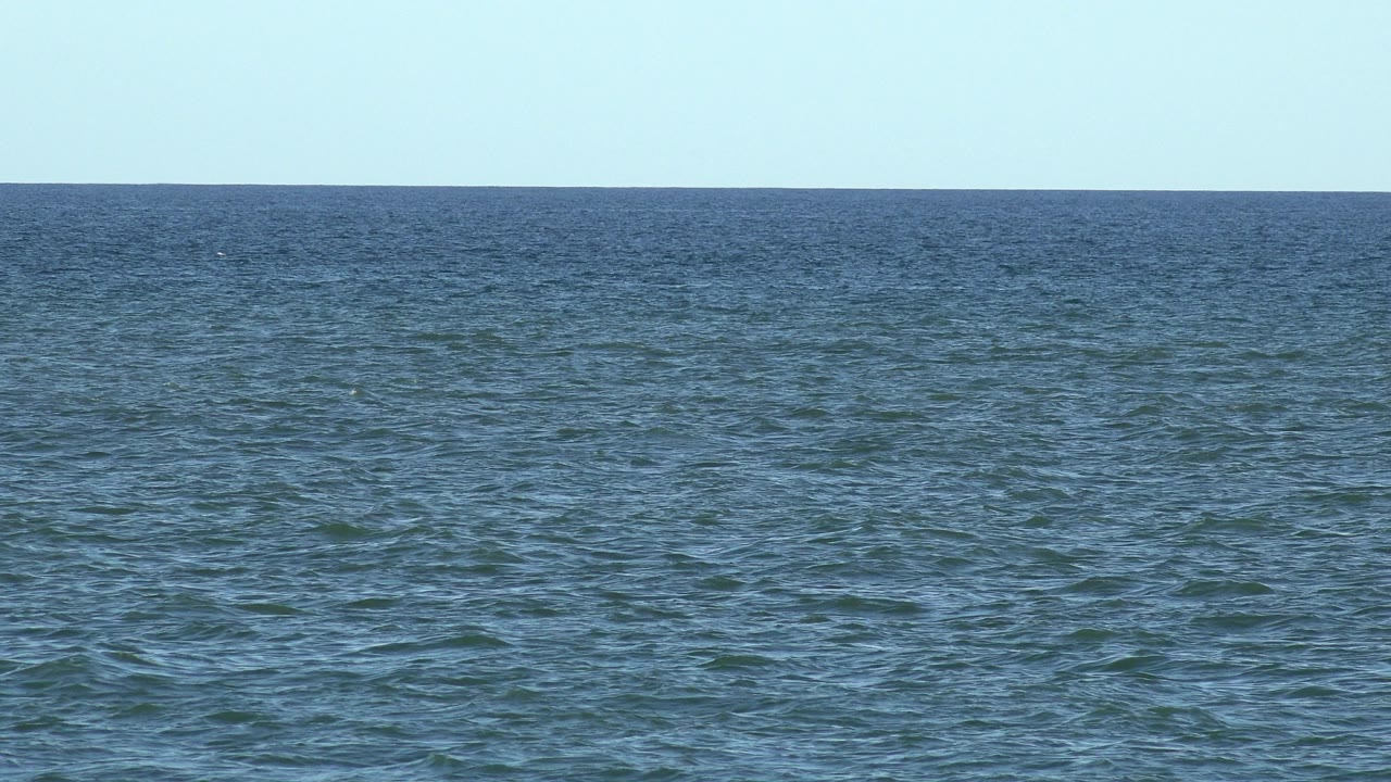 Open Los Cabos ocean surface with low ripples, a level horizon, pale sky, and no visible people.