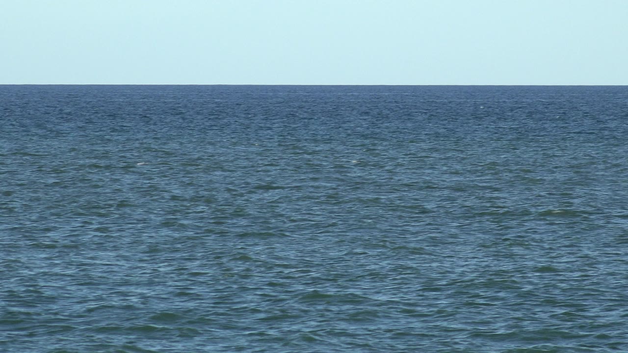 Opening frame of blue open ocean in Los Cabos, Mexico with a straight horizon, pale cloudless sky, and no visible people.