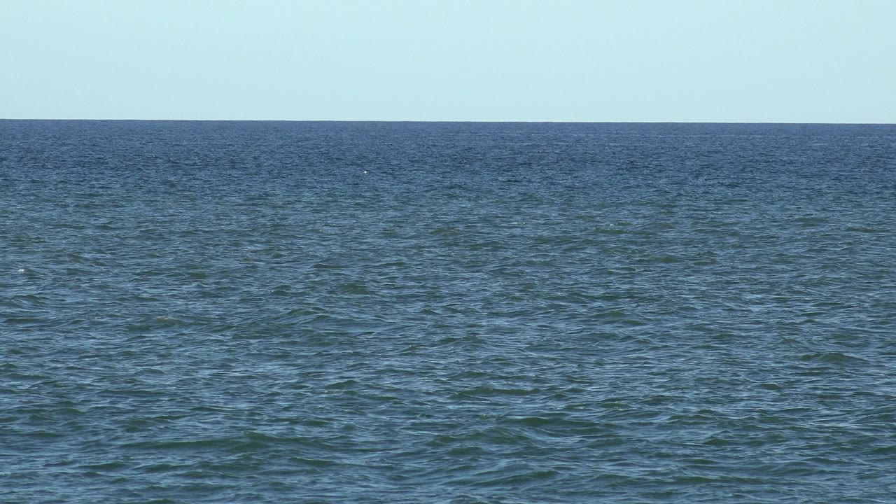 Opening frame of Los Cabos ocean water with small ripples, a level horizon, pale blue sky, and no visible people.