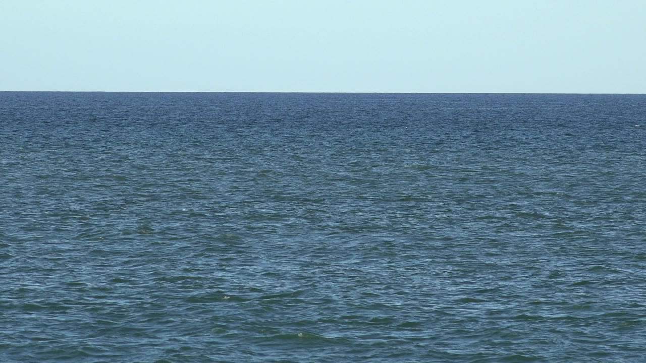 Los Cabos sea view at 0:02 with rippled blue-green water, a flat horizon near the upper frame, bright sky, and no visible people.