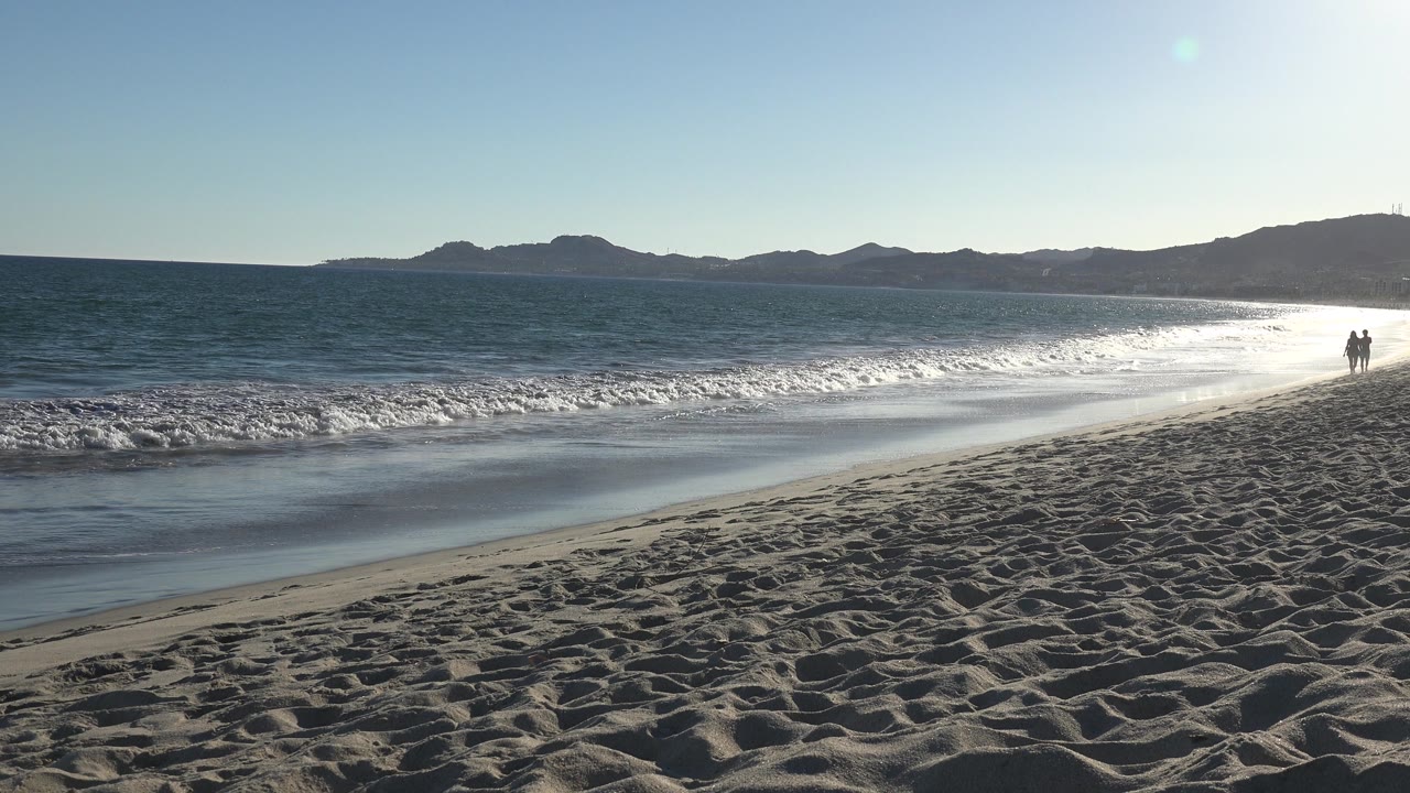 Open beach and ocean with two people walking near the far right edge.
