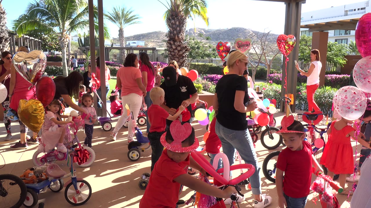 Children and adults at a red and pink decorated party with balloons and small bikes.