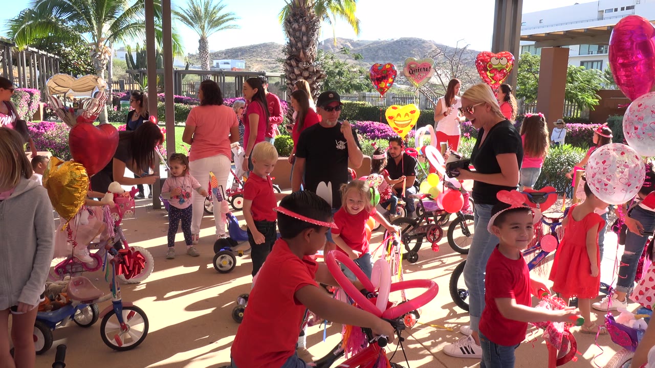 Children and adults at a Valentine's bike party with heart balloons and small bicycles.