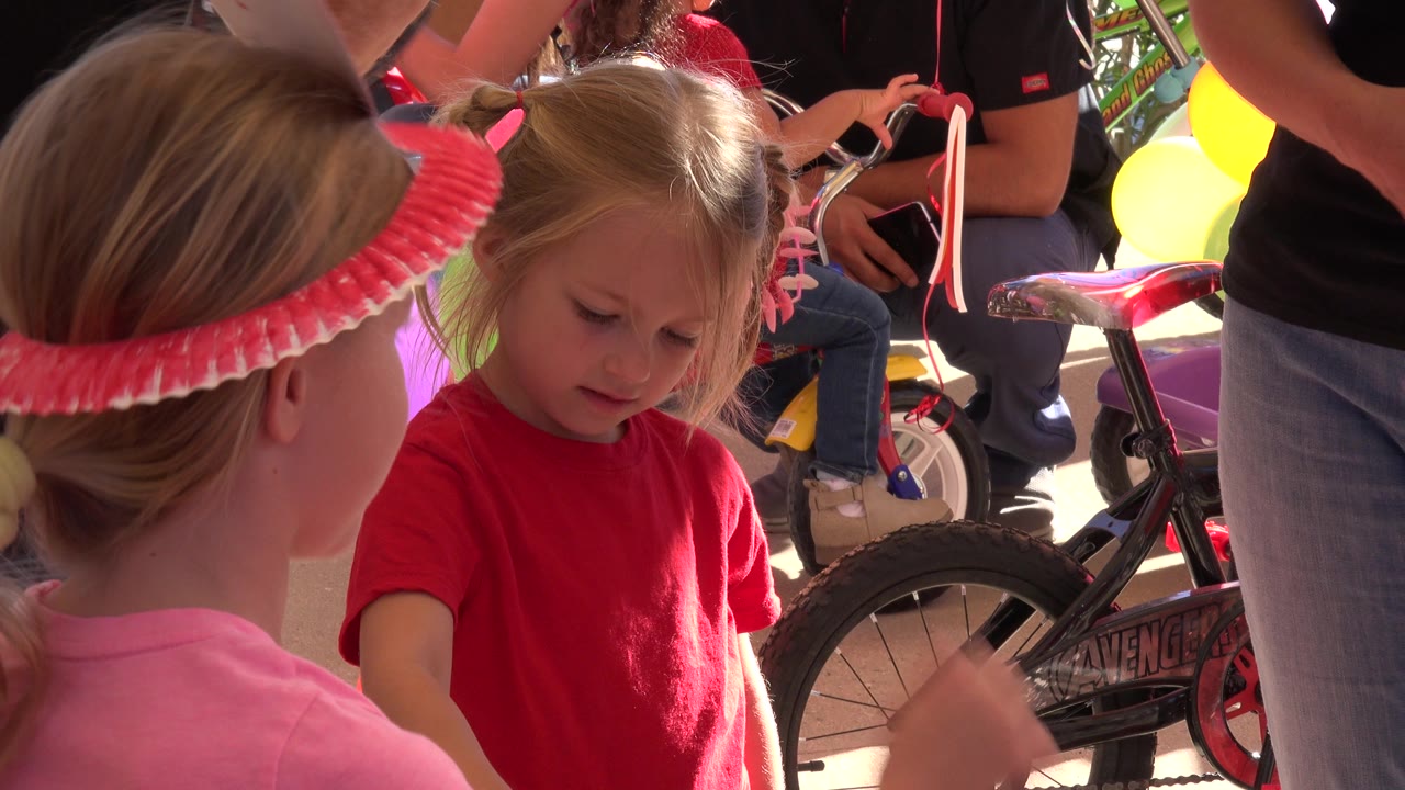 A young girl in a red shirt looks downward while another child in pink stands in the foreground and a children's bicycle sits behind them in Los Cabos, Mexico.