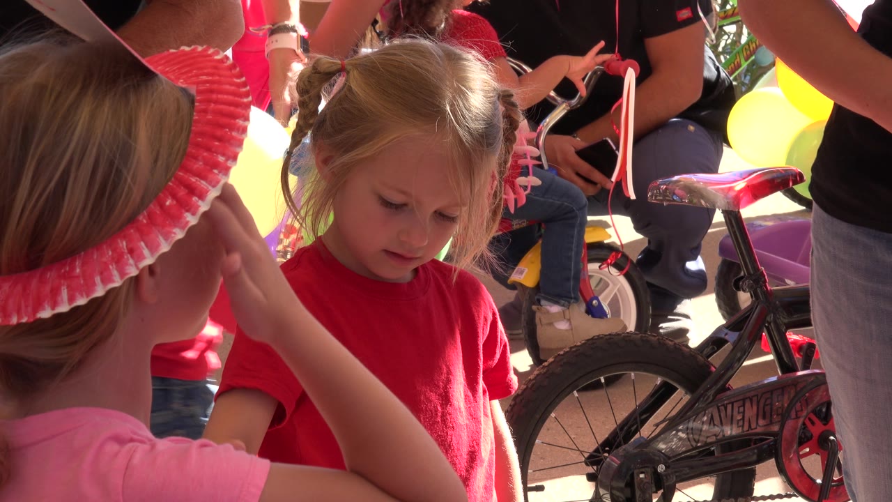 Child adjusts pink headband near girl in red shirt
