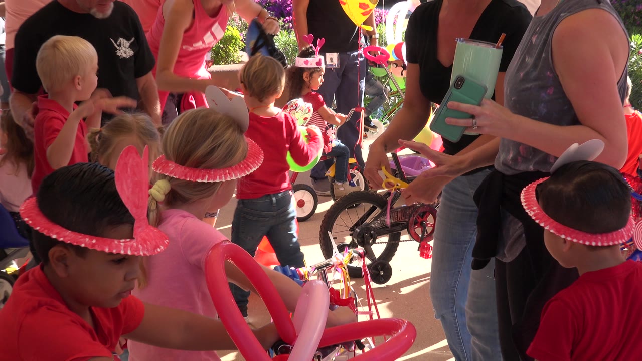 A child in a pink hat sits near bicycle handlebars while other children and adults cluster nearby at the Los Cabos outdoor party.