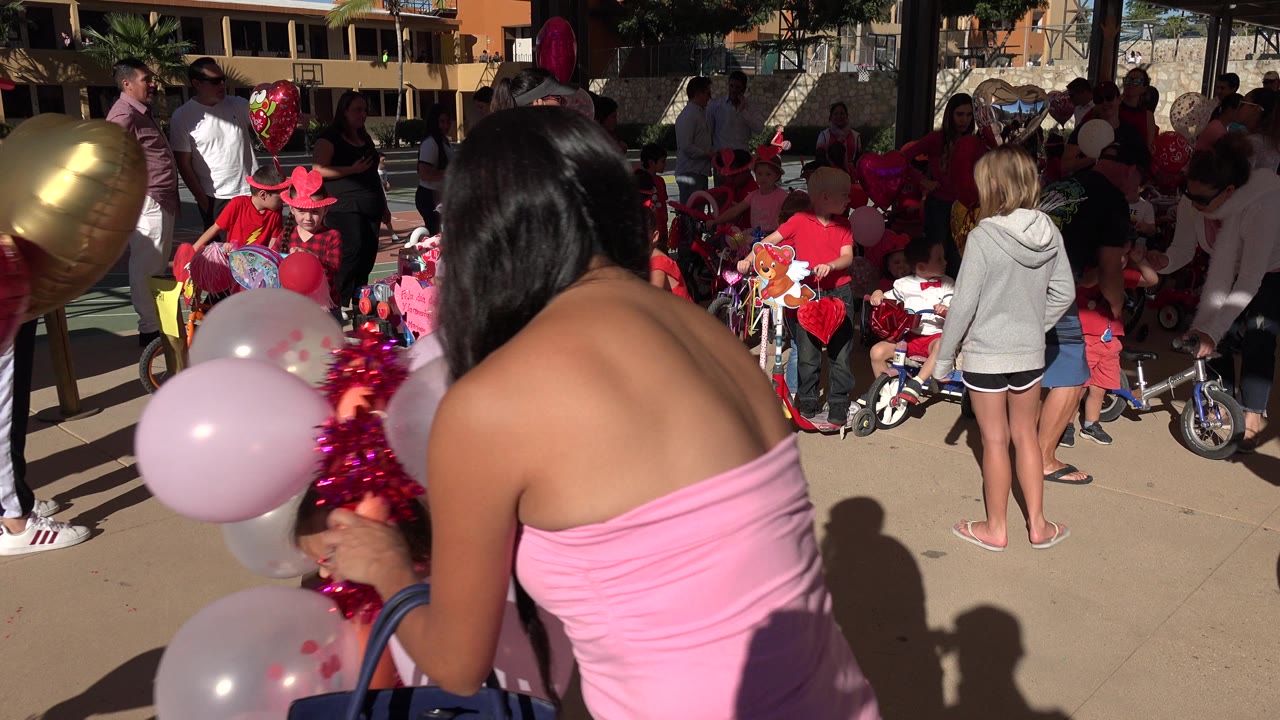 Adults and children gather around balloons and decorated bikes at an outdoor party.