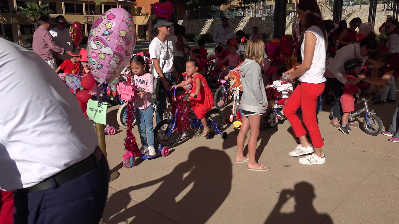 Children and adults gather beside decorated bicycles and balloons on a sunny walkway.