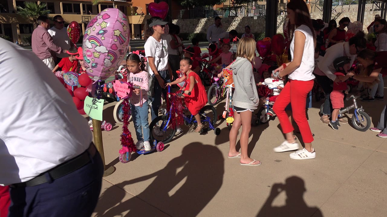 A large pink patterned balloon dominates the left foreground while children and adults remain gathered around decorated bikes in Los Cabos.