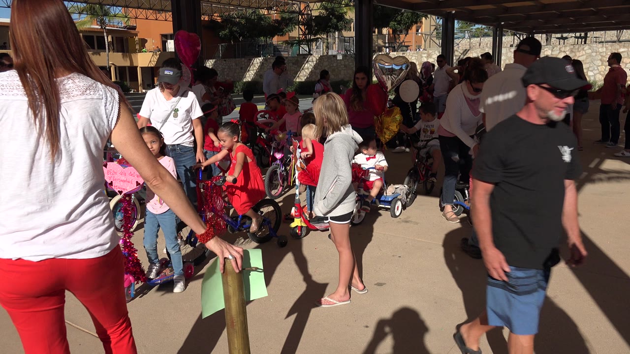Adults and children gather around decorated bikes under shade.