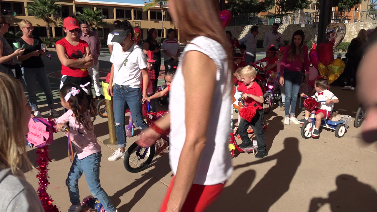 Children and adults gathered around decorated bikes and scooters on a sunny street.