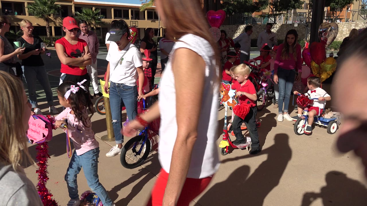 A young girl in a pink top stands near a decorated pink scooter as adults and children gather with small bikes in Los Cabos, Mexico.