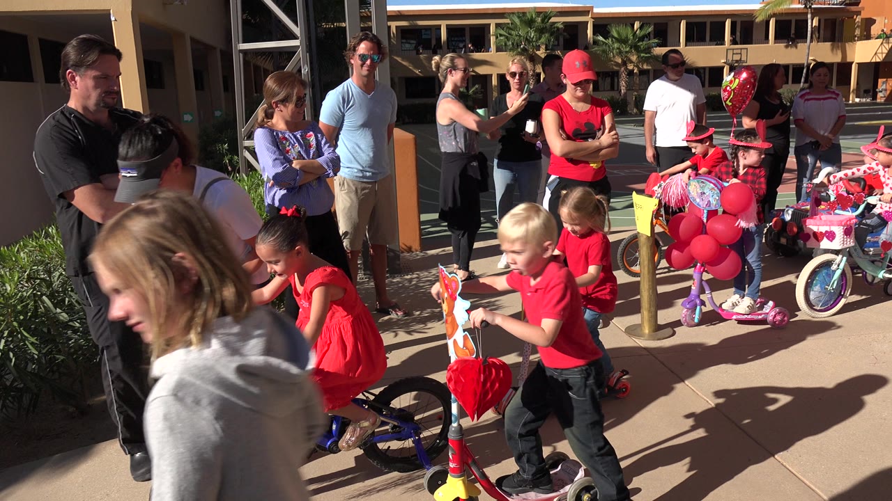 Children ride decorated bikes and scooters while adults watch nearby.