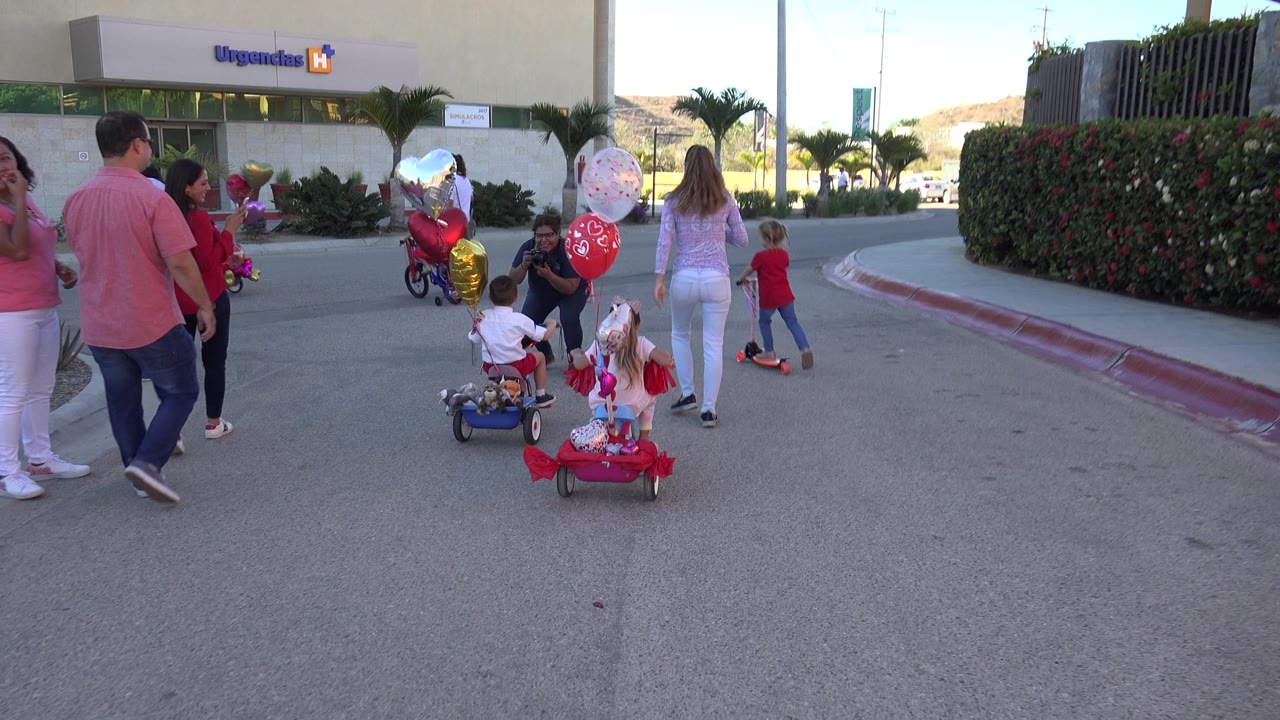 Adults and children move near balloon-covered bikes outside a building.