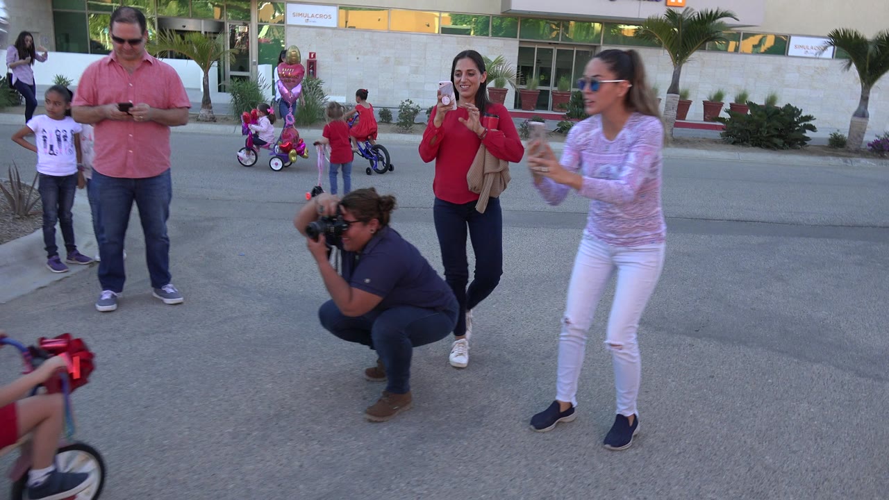 Adults filming children on a street while a photographer crouches nearby.