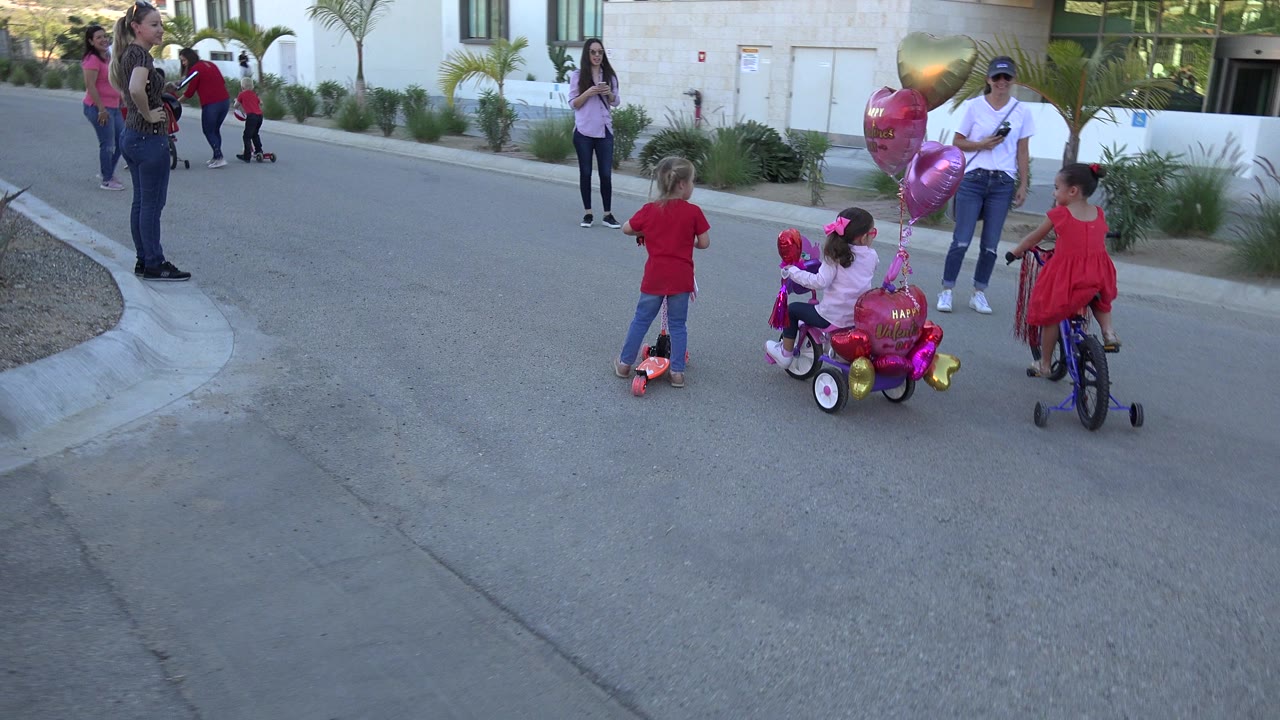 The children begin spreading out along the paved lane as a seated adult holds balloons near the curb in Los Cabos, Mexico.