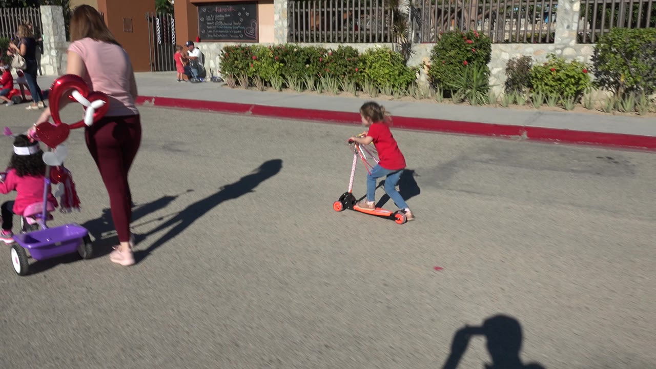 Woman and child with ride-on toy near girl pushing scooter.